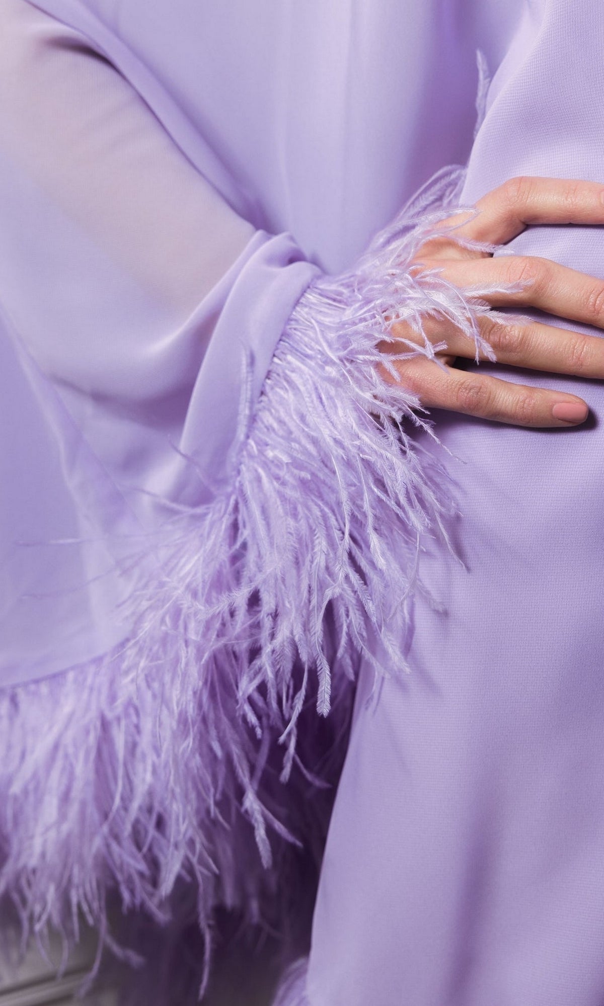 A close-up of a person wearing the Short Wedding Guest Dress: Mac Duggal 11623 in lavender, featuring feathered sleeve trim, with their hand resting gently on the fabric.